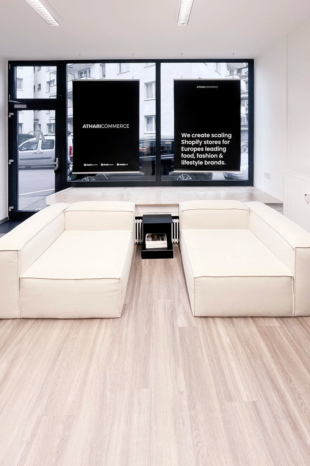 Büroraum von AthariCommerce in Köln mit beigen Sofas und dem Markenauftritt im Schaufenster