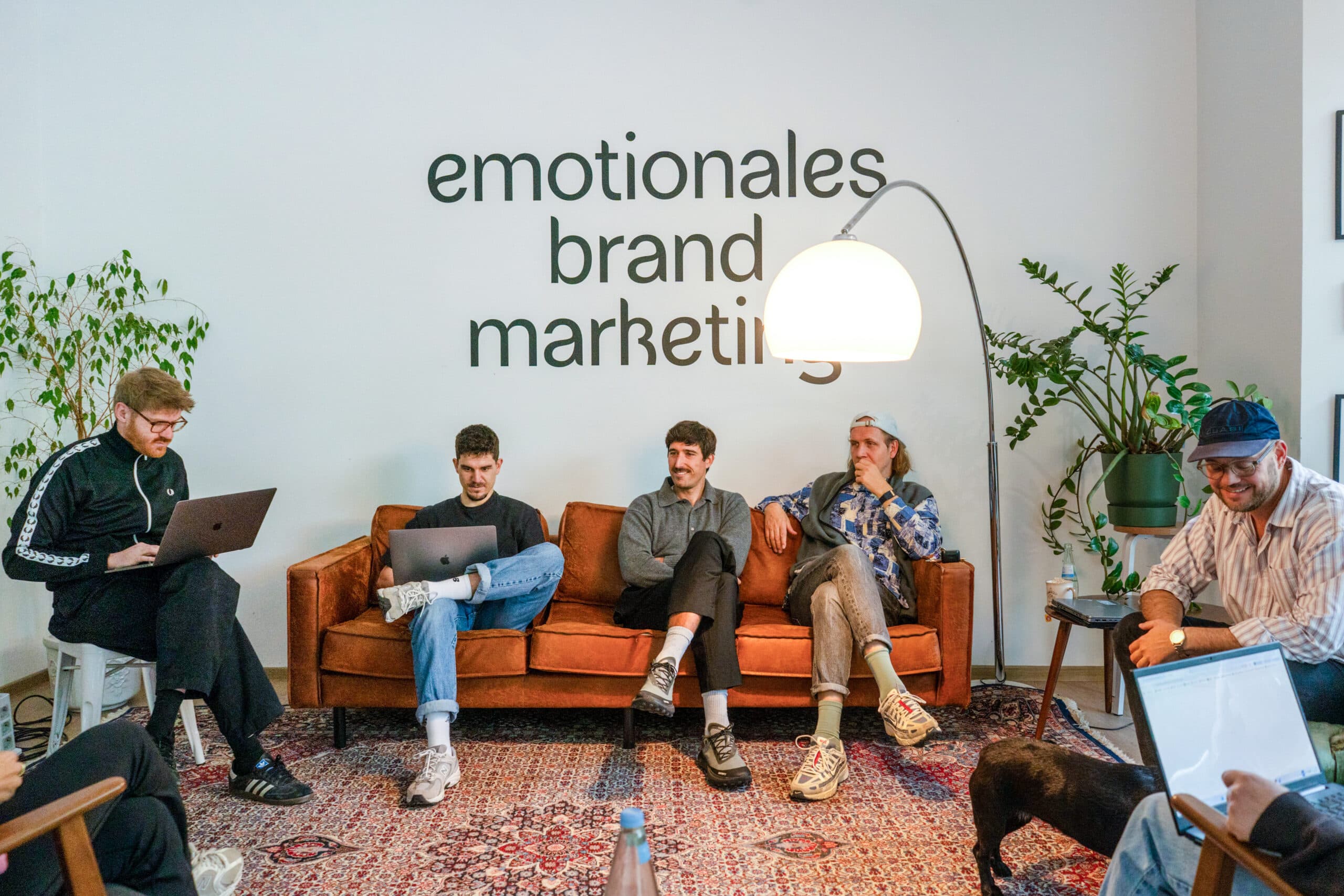 Das farbenkollektiv-Team im Kölner Büro vor der Wandschrift „emotionales brand marketing“