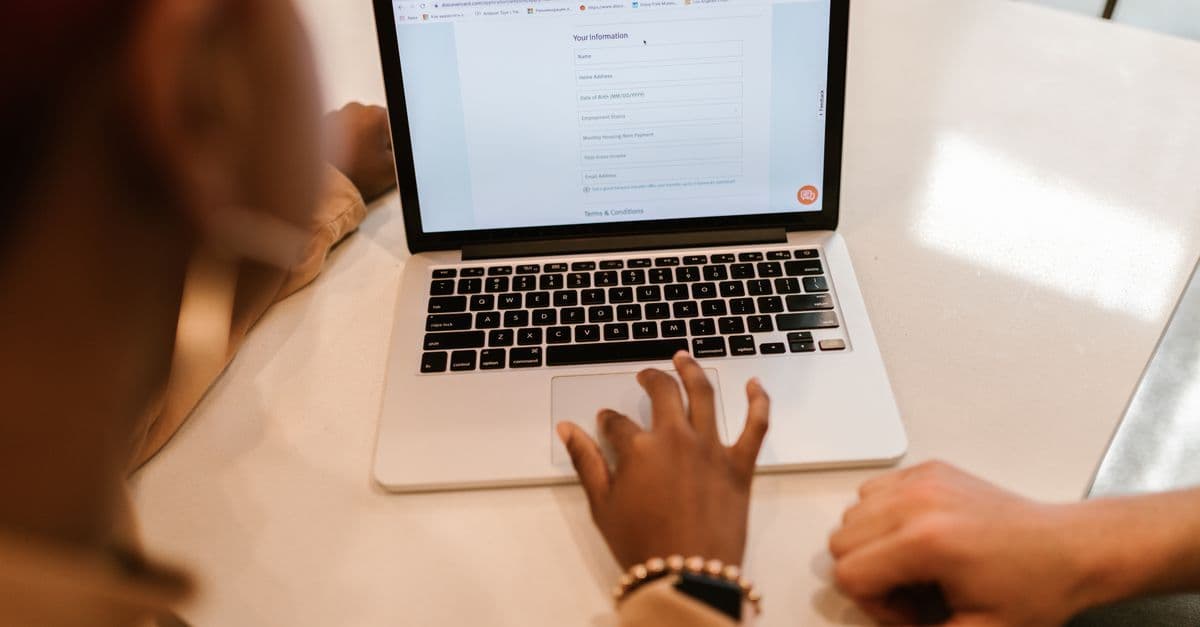 Zwei Erwachsene bearbeiten gemeinsam an einem Laptop ein Online-Formular im Innenraum.