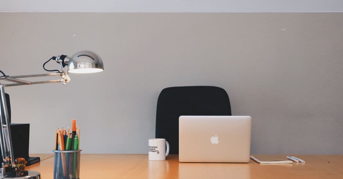 Aufgeräumter minimalistischer Schreibtisch mit Laptop, Lampe und Schreibutensilien