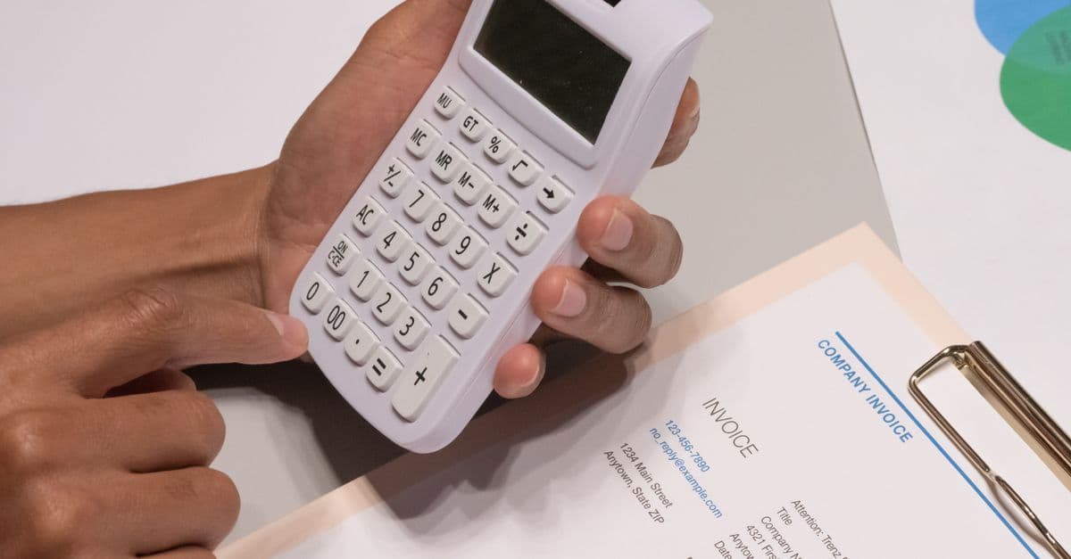 Hände mit Taschenrechner neben einer Firmenrechnung bei einer Finanzberechnung
