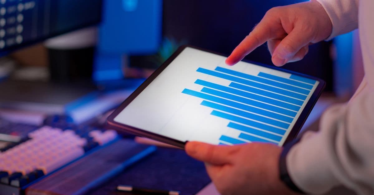 Geschäftsperson analysiert Balkendiagramm auf einem Tablet im Büro und markiert auffällige Datenwerte.