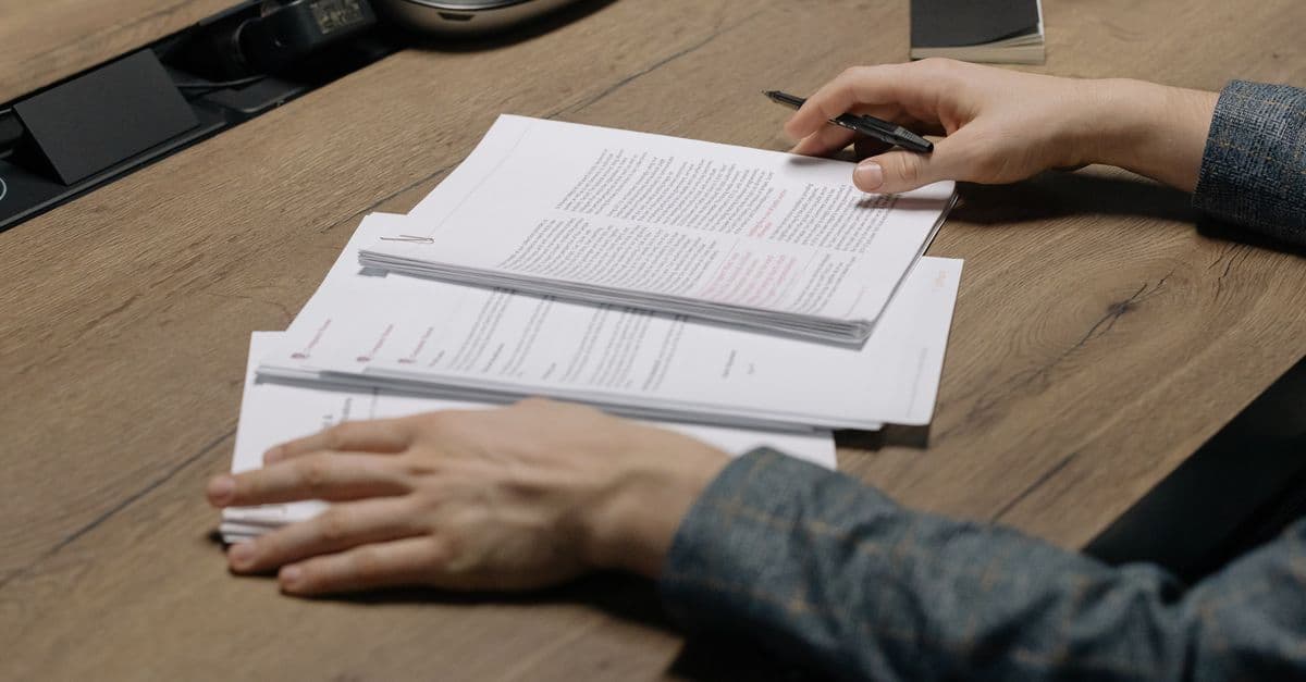 Person prüft Unterlagen mit Stift an einem modernen Büroschreibtisch.
