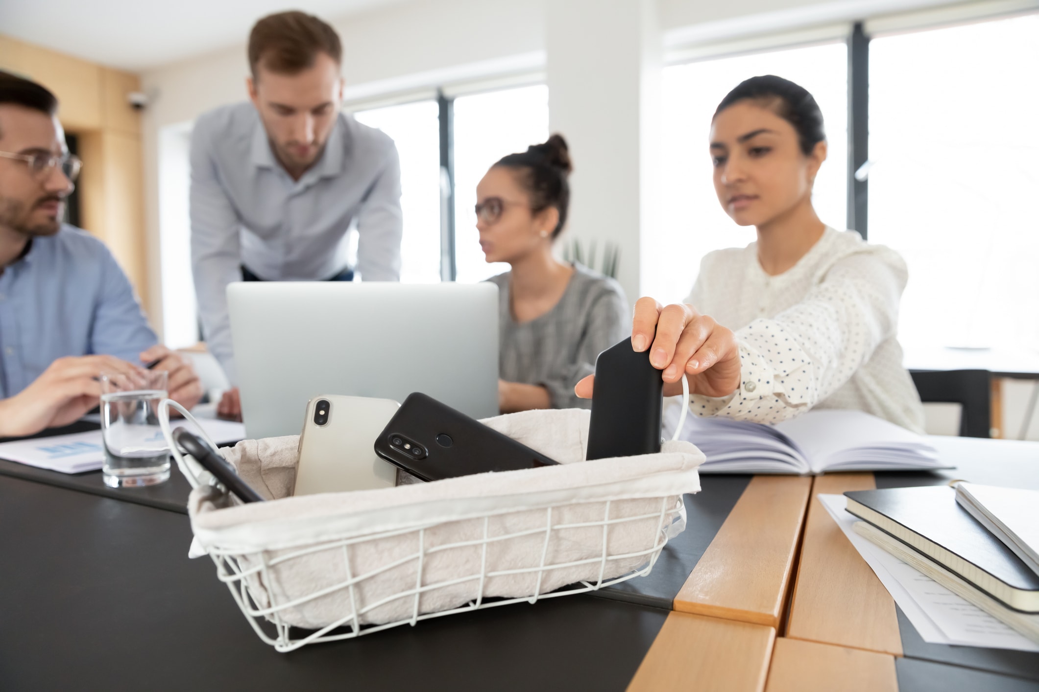 Mitarbeiterin legt ein schwarzes Smartphone vor einer Besprechung in eine Box.